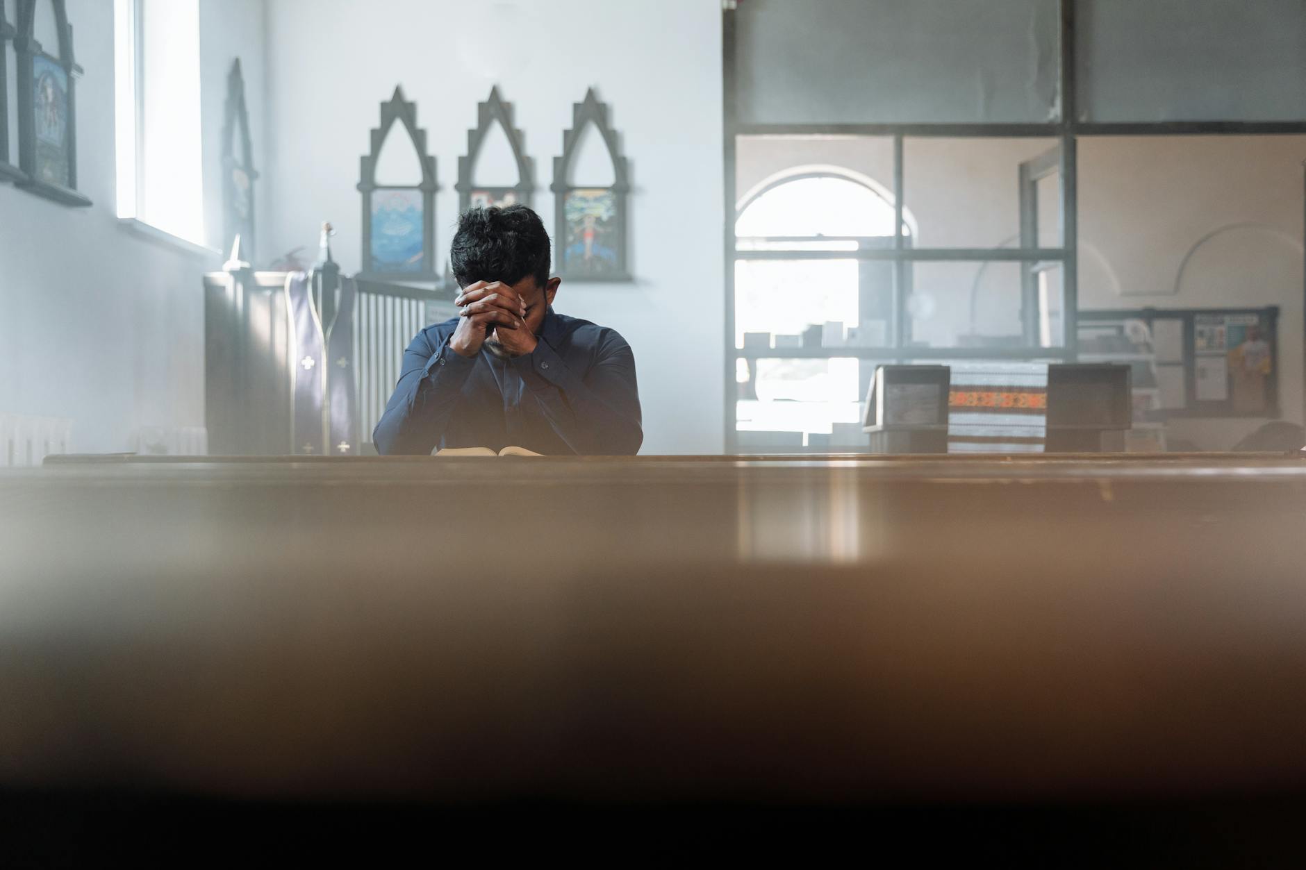 Mężczyzna modlący się w słonecznym pokoju, pogrążony w zadumie