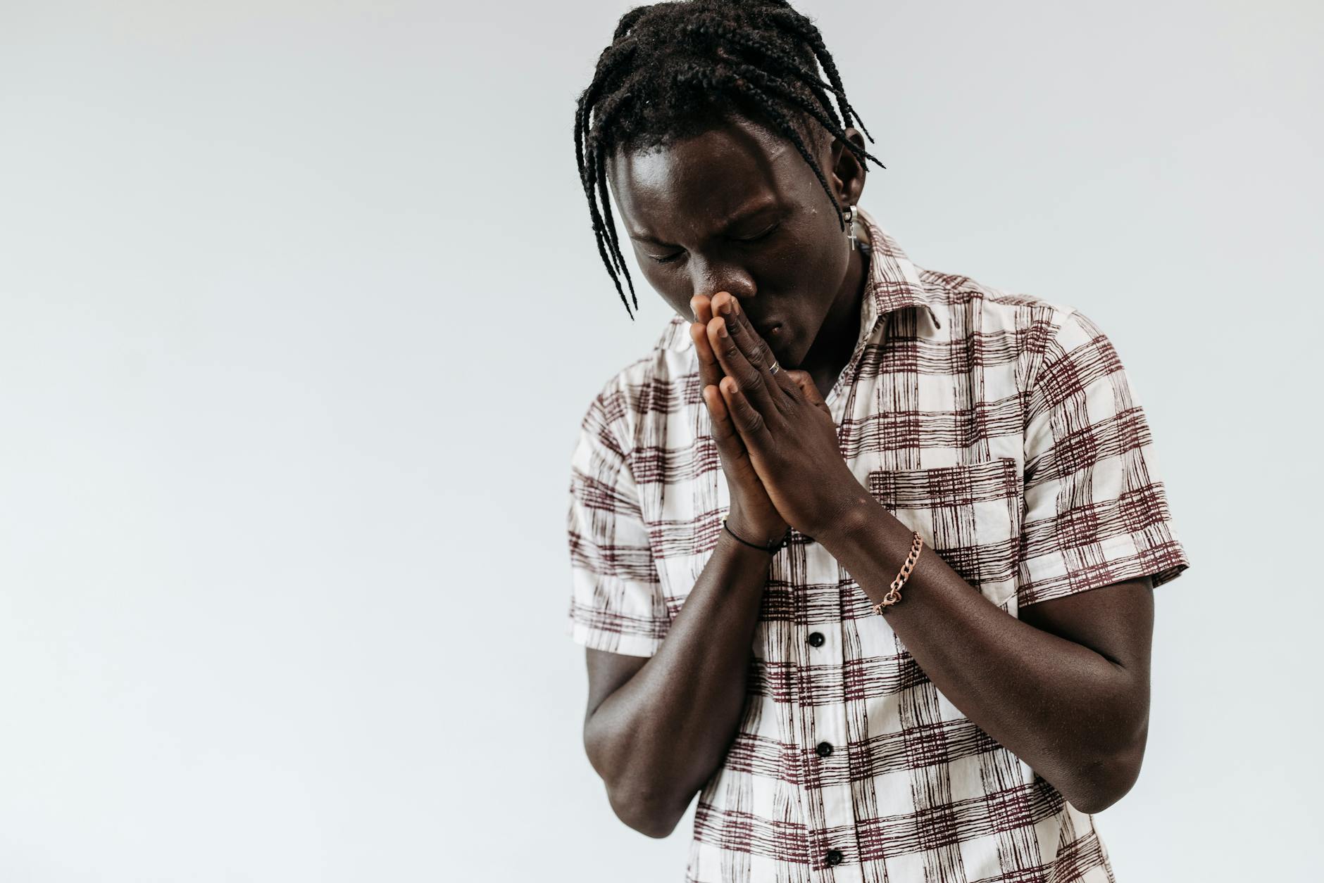Młody mężczyzna w koszuli w kratę modli się na białym tle