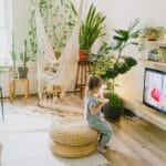 Rośliny jako element projektu wnętrza: jak dobierać gatunki do światła, stylu i trybu życia Dziecko z przekąską w salonie pełnym roślin i wiszącym fotelem